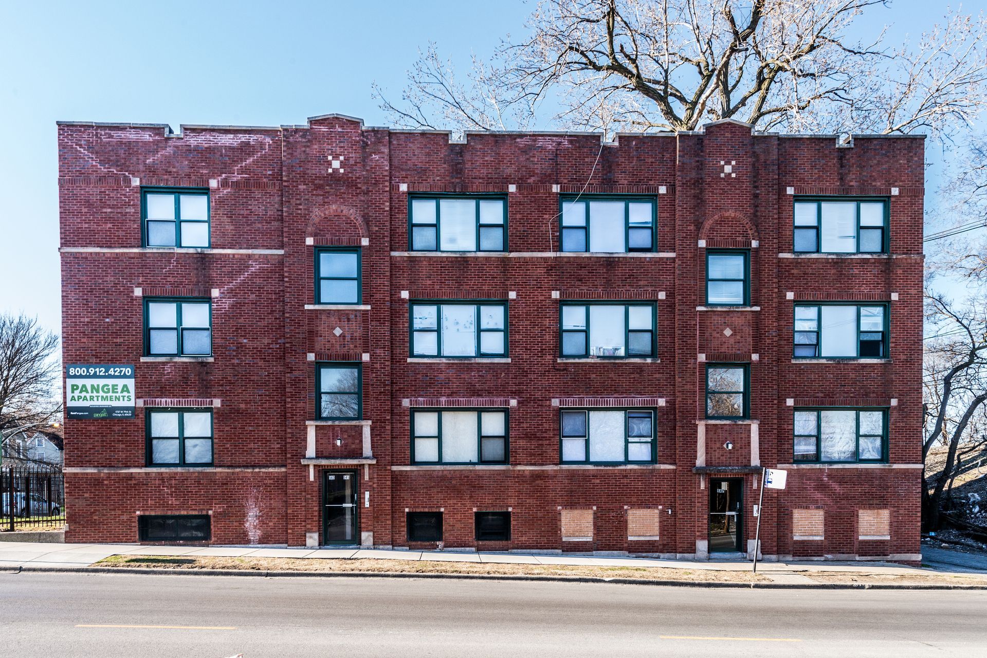Three-story brick apartment building with dark trim, windows, and two entry doors.