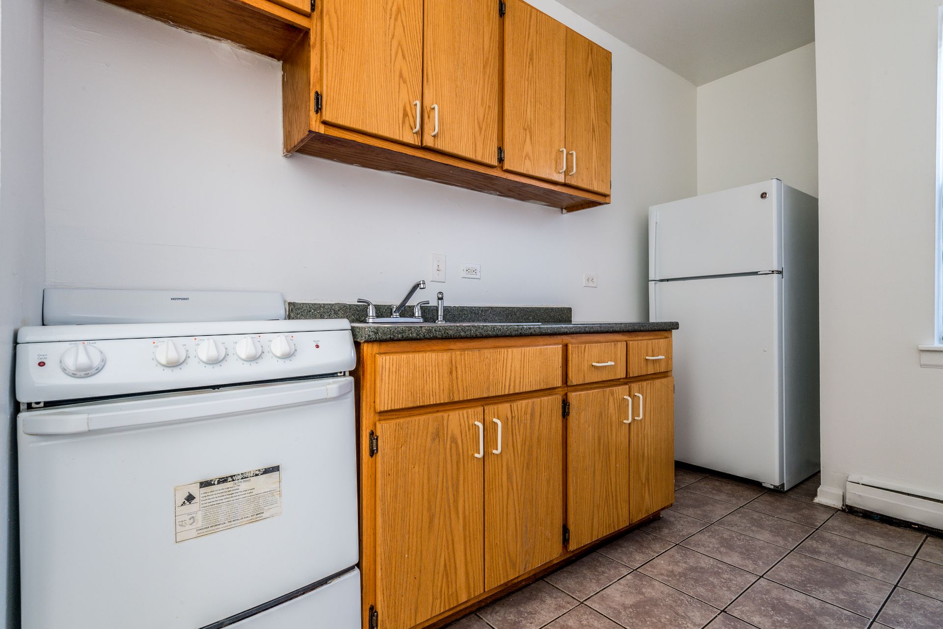 Small kitchen with wood cabinets, white appliances, and a window.
