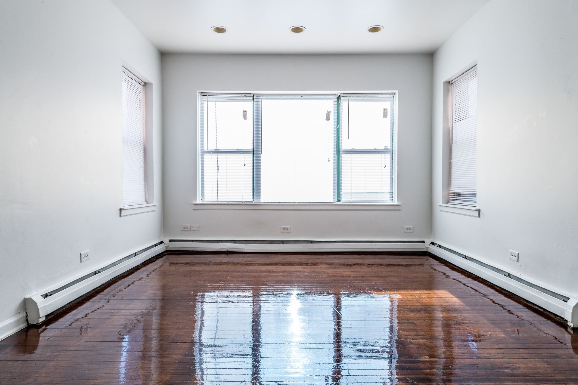 Empty room with hardwood floors, a large window, and two smaller side windows.