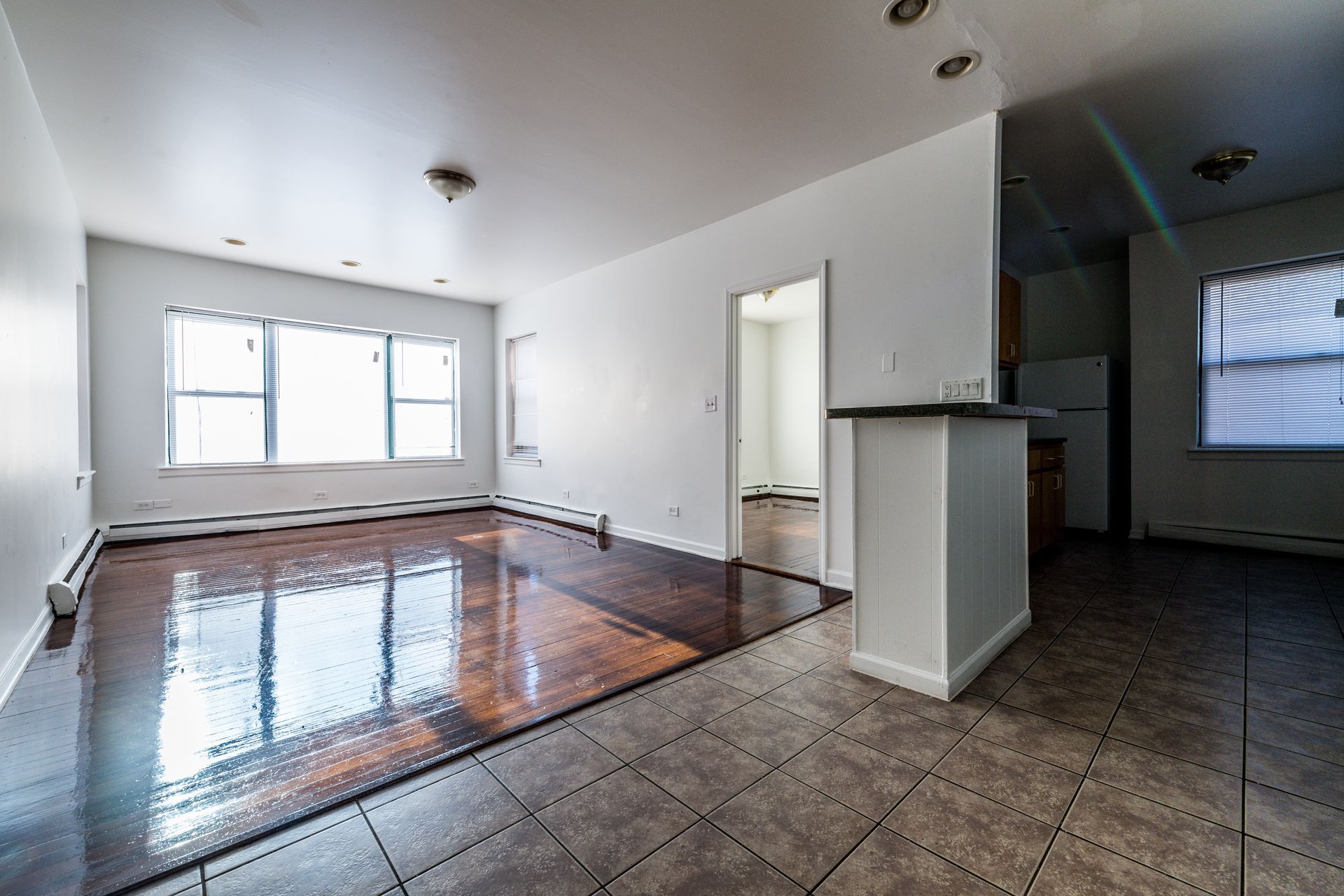 Empty interior with hardwood floors, white walls, and a small kitchen area.