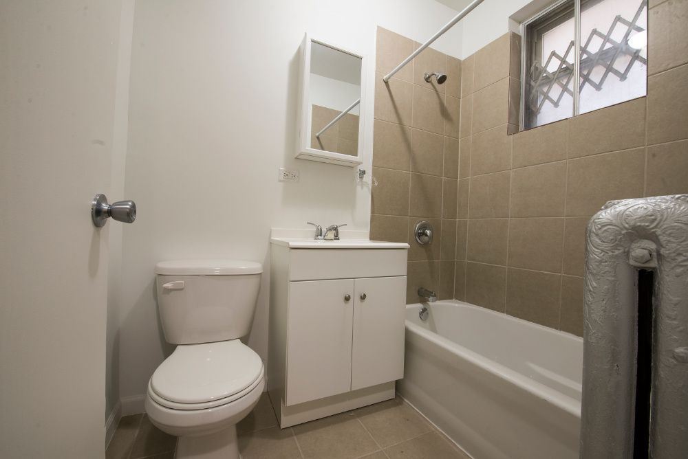 Bathroom with toilet, sink, tub with tile surround, and radiator.