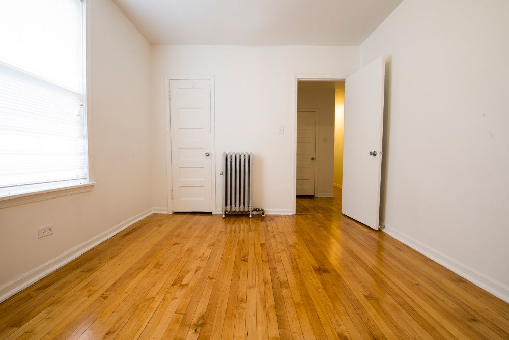 Empty room with hardwood floors, white walls, and two doors.