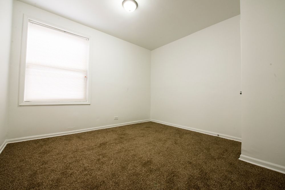Empty room with brown carpet, white walls, a window with blinds, and a ceiling light.