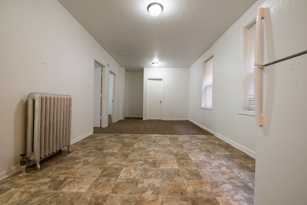 Empty room with radiator, brown tiled floor, white walls, and two doorways.