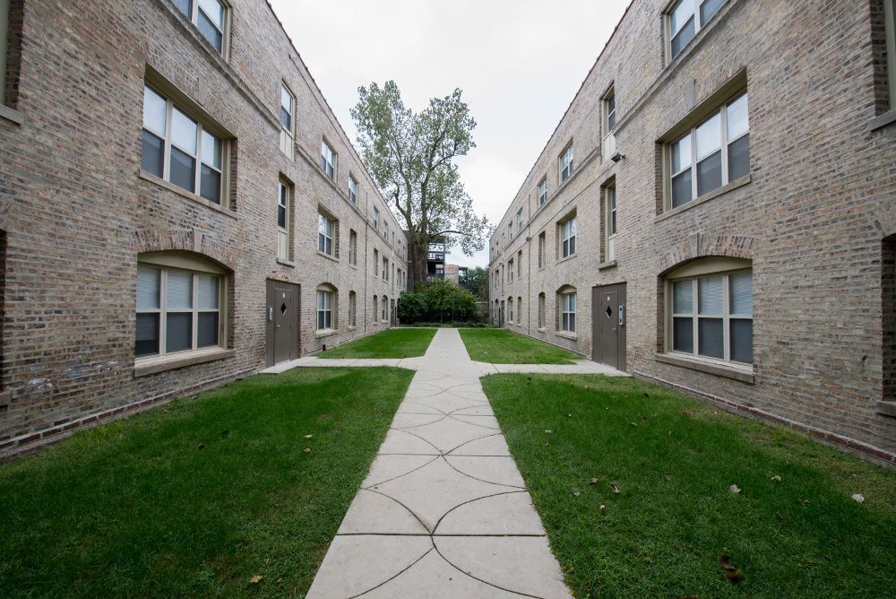 Two brick apartment buildings face each other, with a grassy courtyard and a paved walkway.