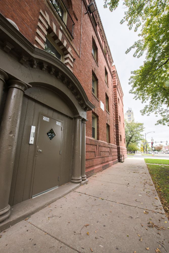Brick building with arched doorway and sidewalk, overcast day.