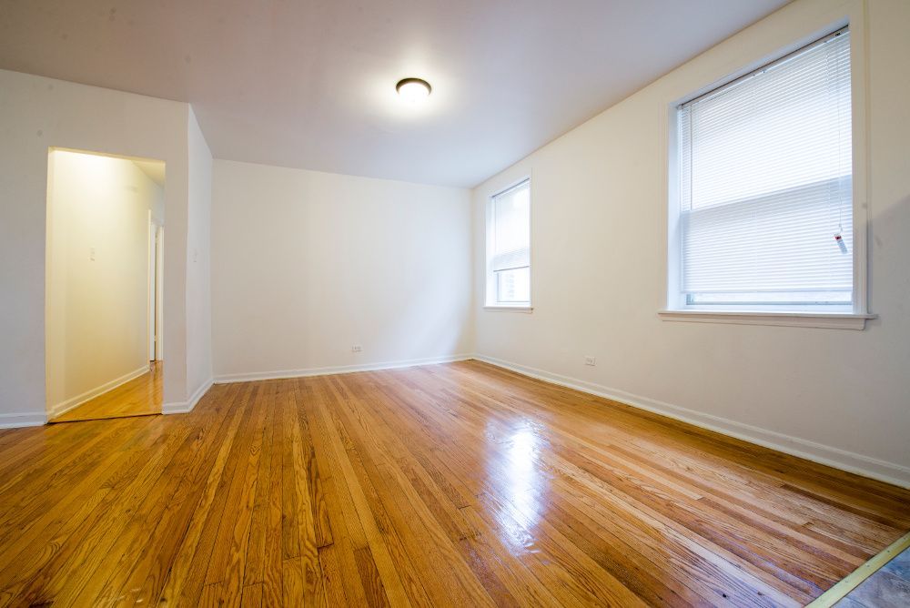 Empty room with hardwood floors, white walls, two windows, and overhead light.