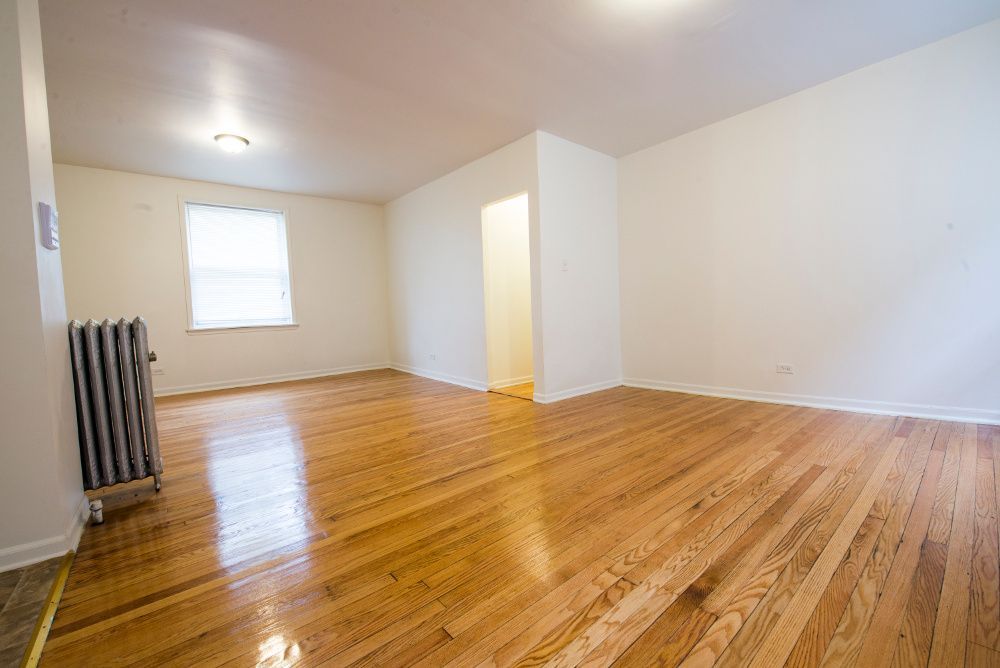 Empty room with hardwood floors, radiator, window, and an entrance to another space.