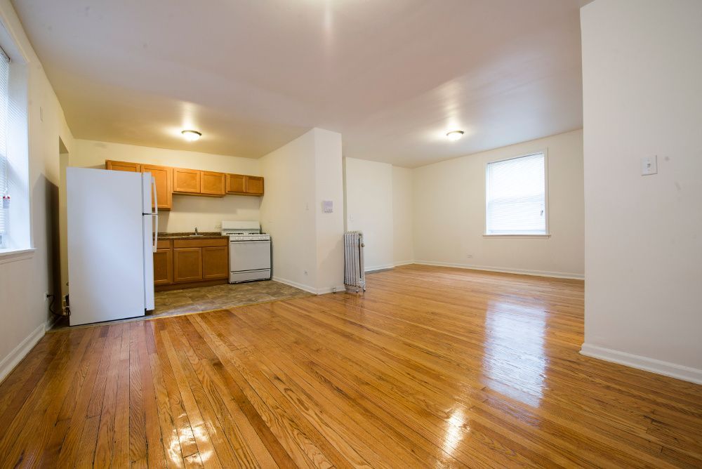 Empty apartment interior with wooden floors, kitchen, and windows.