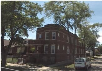 Brick apartment building on a street lined with trees, sunny day. A van is parked on the street.