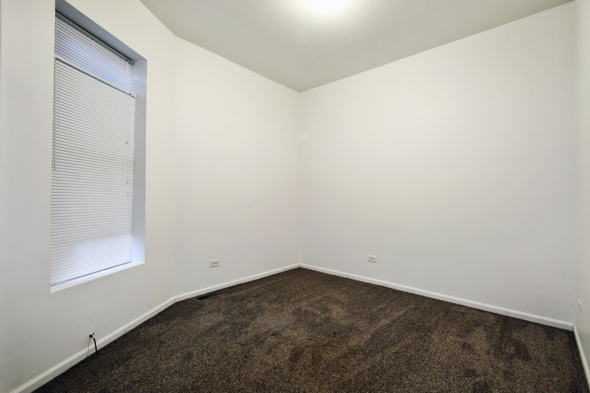 Empty room with brown carpet, white walls, and a window with a light-colored shade.