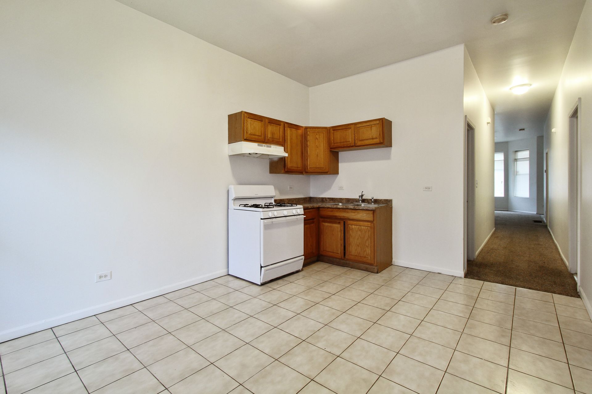 Small kitchen with white appliances, wooden cabinets, and tile floor.