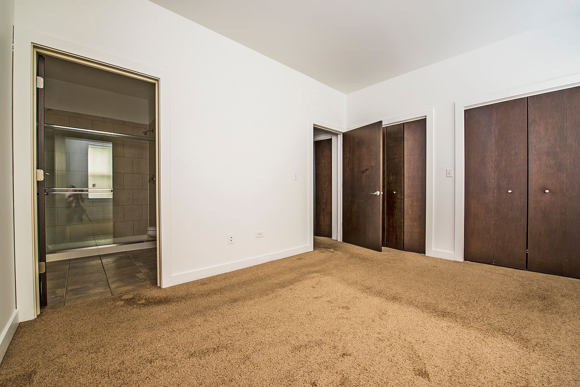 Empty room with brown carpet, white walls, and dark brown closet doors and doorways.