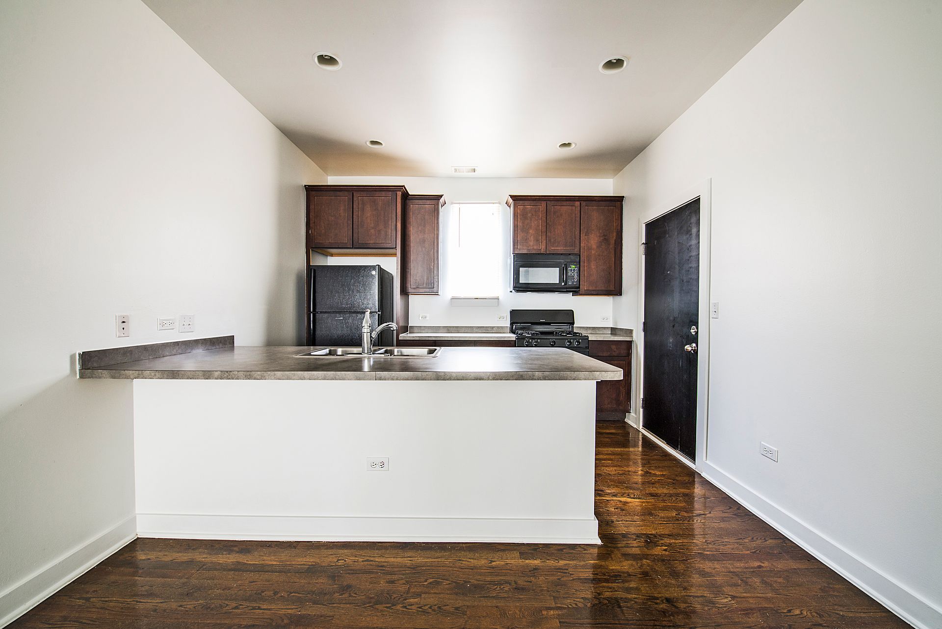 Empty kitchen with dark brown cabinets, appliances, and island; hardwood floor.