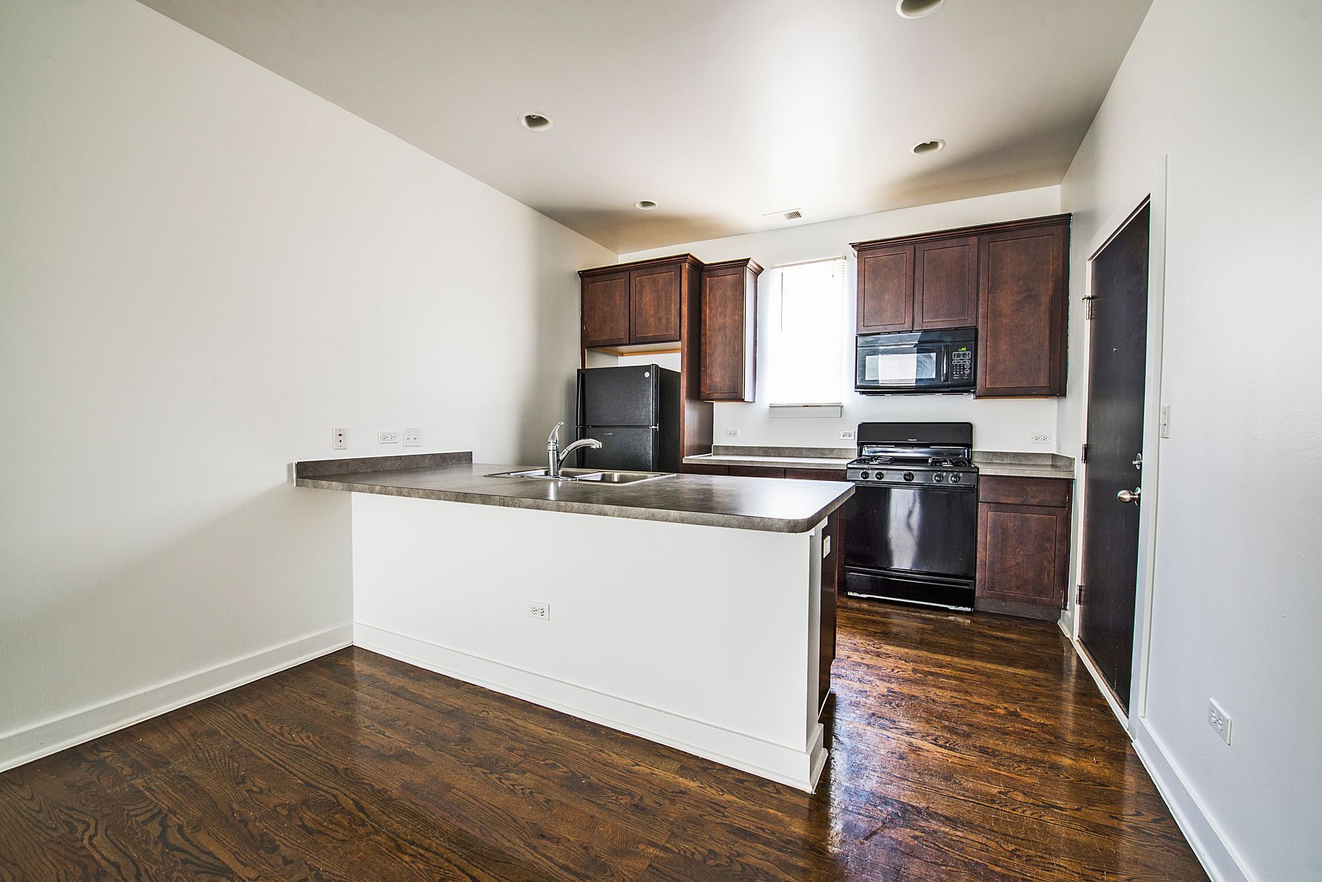 Kitchen with dark cabinets, stainless steel appliances, and wood flooring.