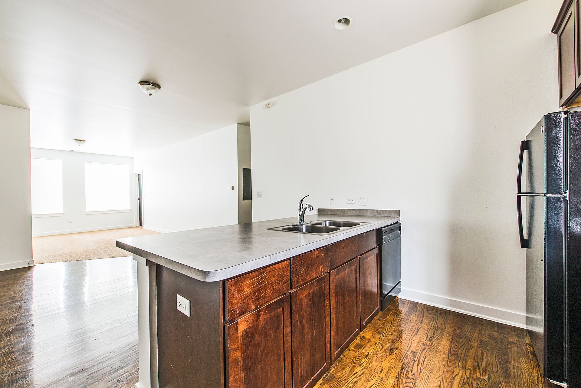 Kitchen with an island, cabinets, and a black refrigerator; hardwood floors.