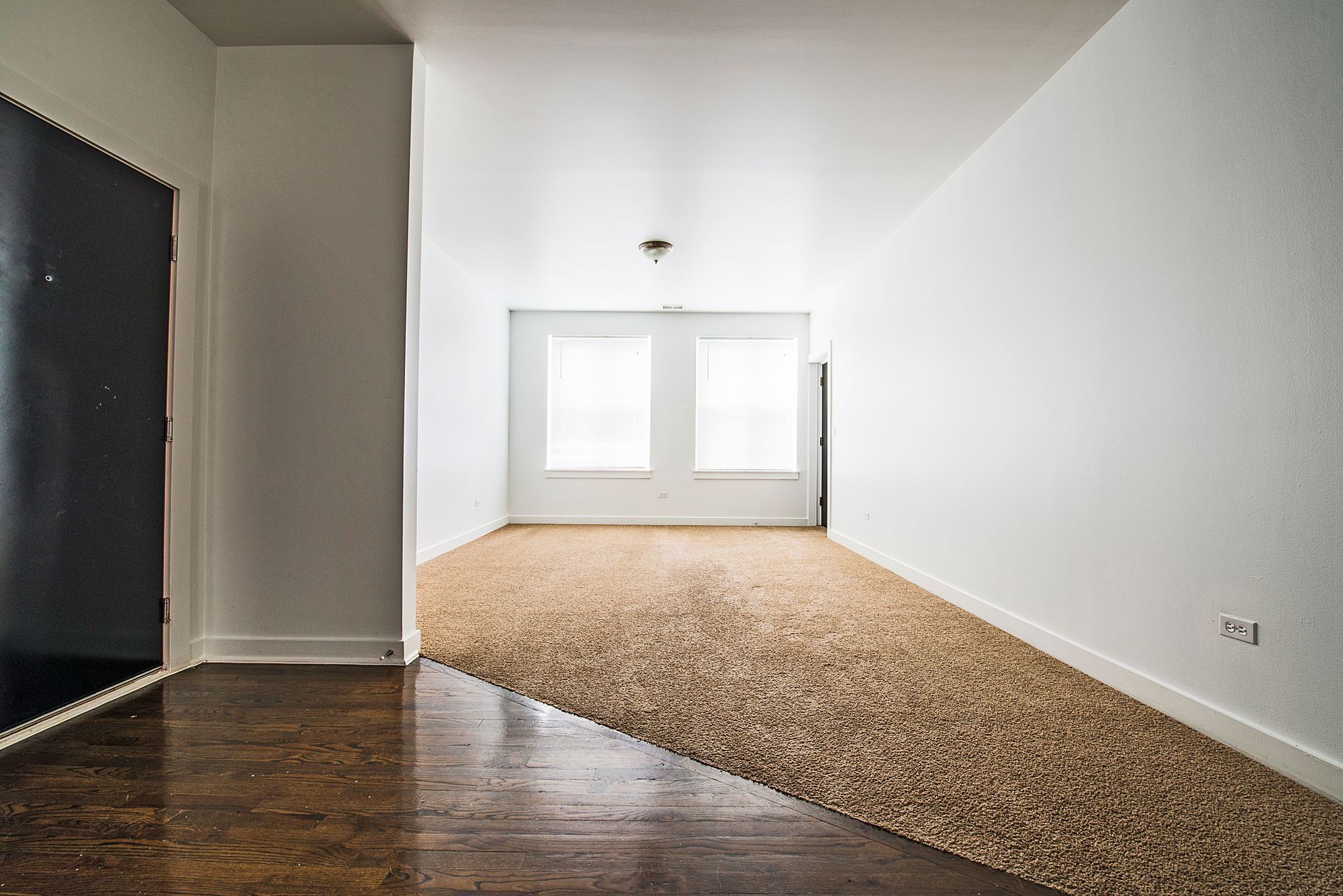 An empty room with hardwood floors transitioning to a gravel-covered area, leading to a window.