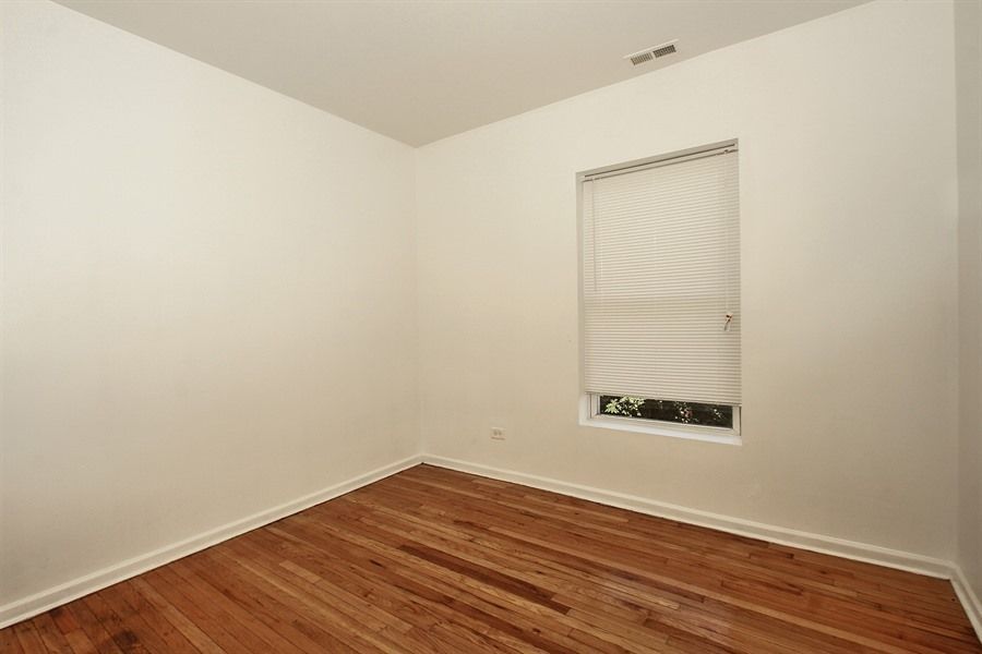 Empty room with hardwood floors, white walls, and a window with blinds.