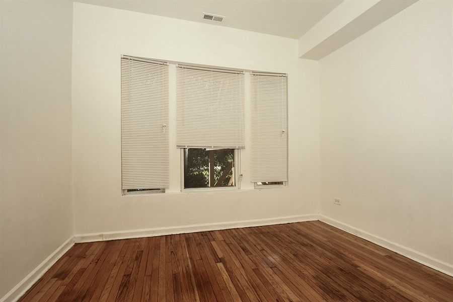 Empty room with hardwood floors, a window with blinds, and white walls.