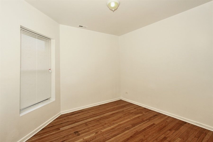 Empty room with hardwood floors, a window with blinds, and a ceiling light.
