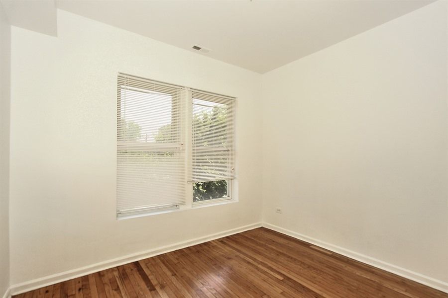 Empty room with hardwood floors, a window with blinds, and white walls.