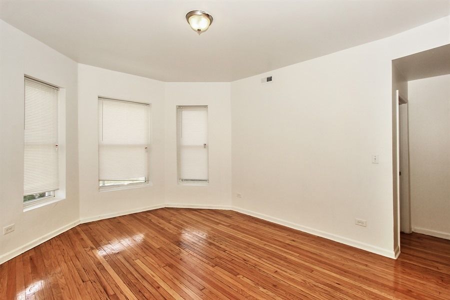 Empty room with hardwood floors, three windows with blinds, and a doorway.