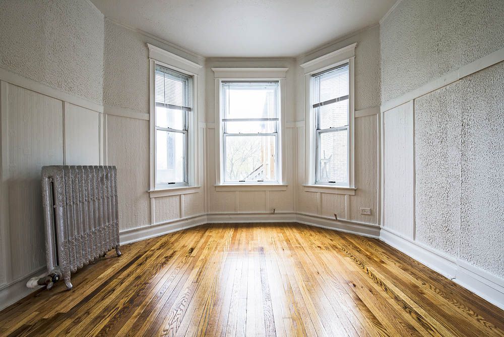 Empty room with hardwood floors, a bay window, and a radiator.