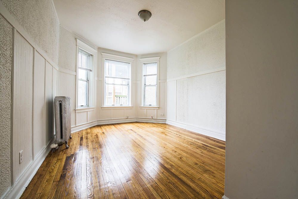 Empty room with hardwood floors, white walls, and a bay window.