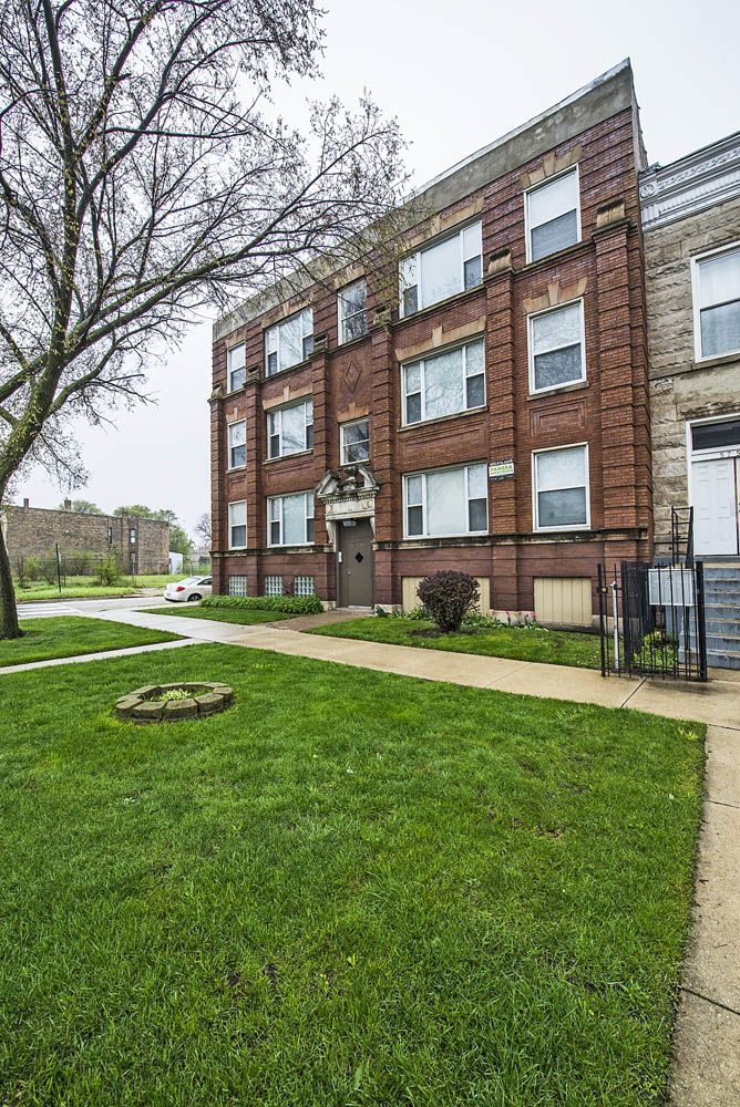 Brick apartment building with green lawn, sidewalk, and cloudy sky.