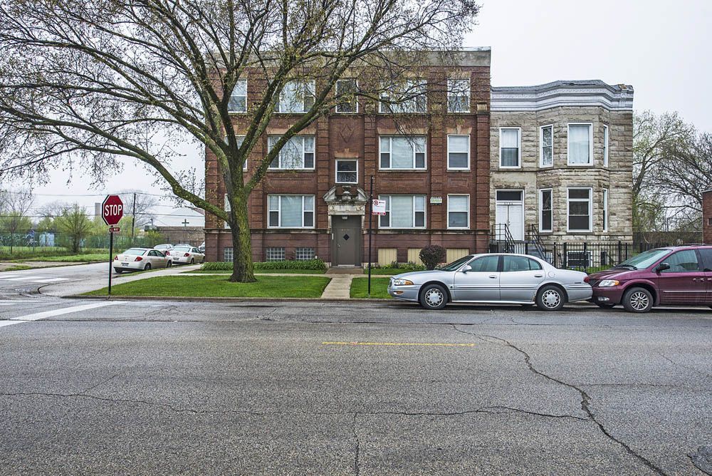 Brick apartment building with parked cars on a city street. A tree stands in front.