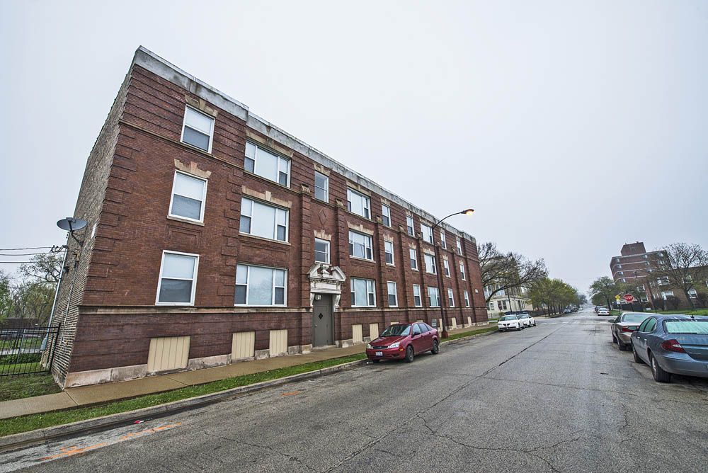 Brick apartment building on a sloped street; cars parked in front. Overcast day.