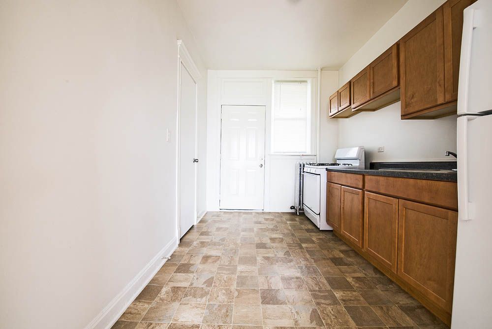 Empty kitchen with brown cabinets, white appliances, and linoleum flooring.