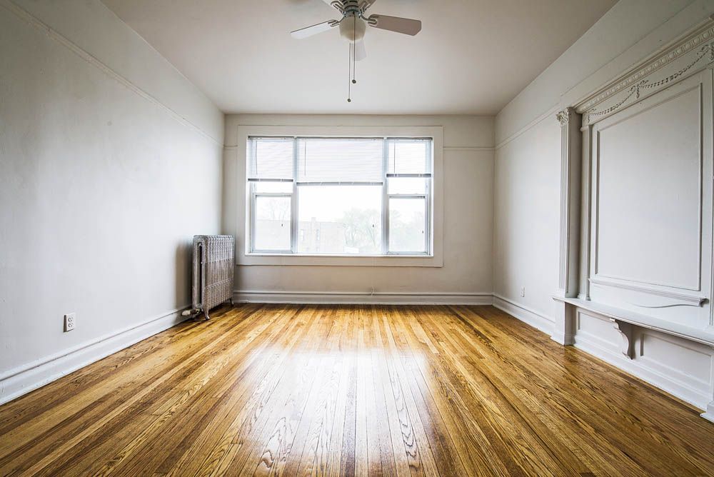 Empty room with hardwood floors, a window, radiator, and ceiling fan. White walls and trim.