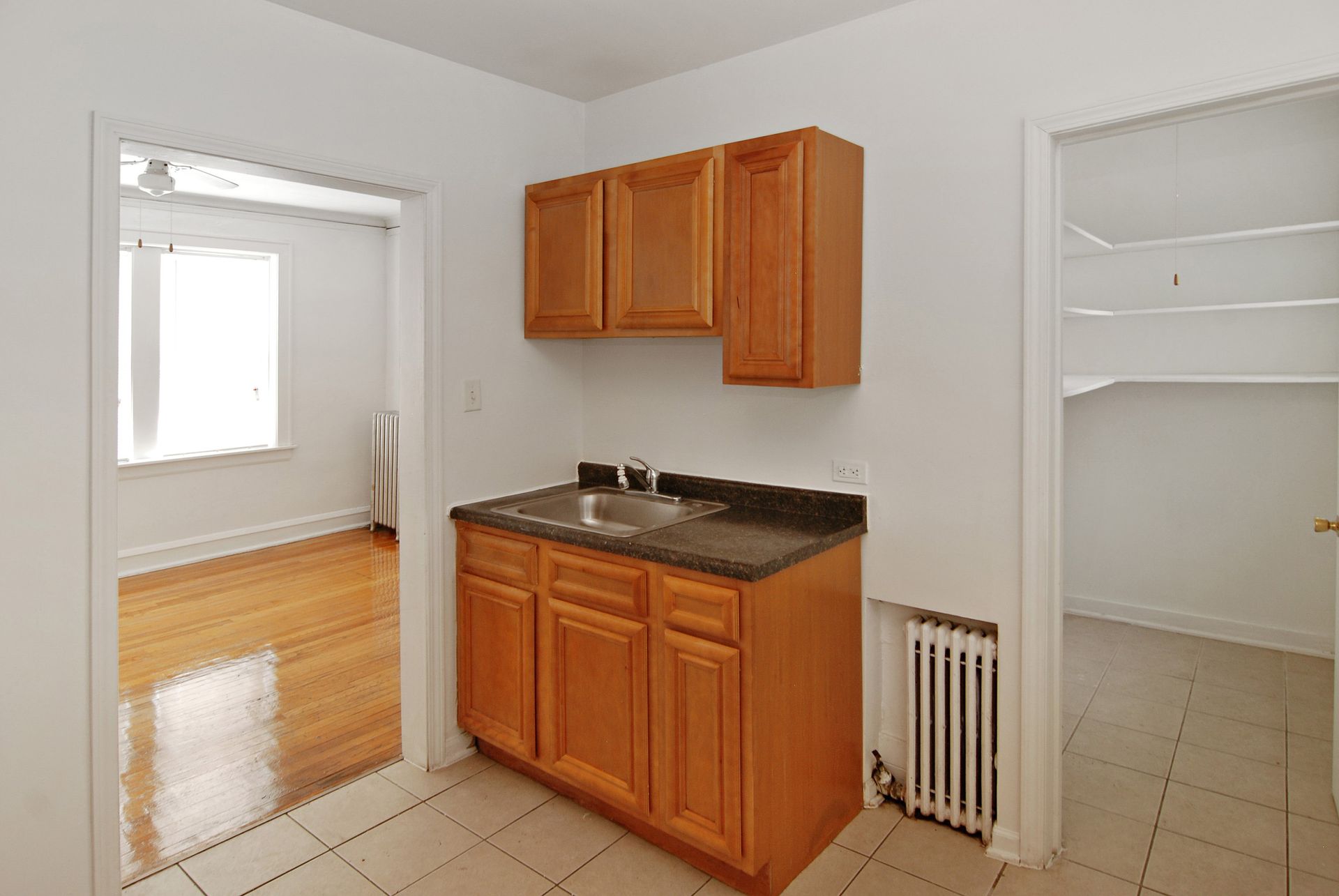 Kitchen with wood cabinets, sink, and doorway to living area; doorway to a pantry.