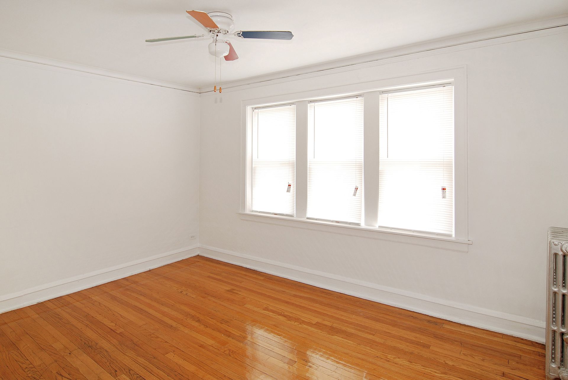 Empty room with hardwood floors, white walls, and a multi-pane window with blinds.
