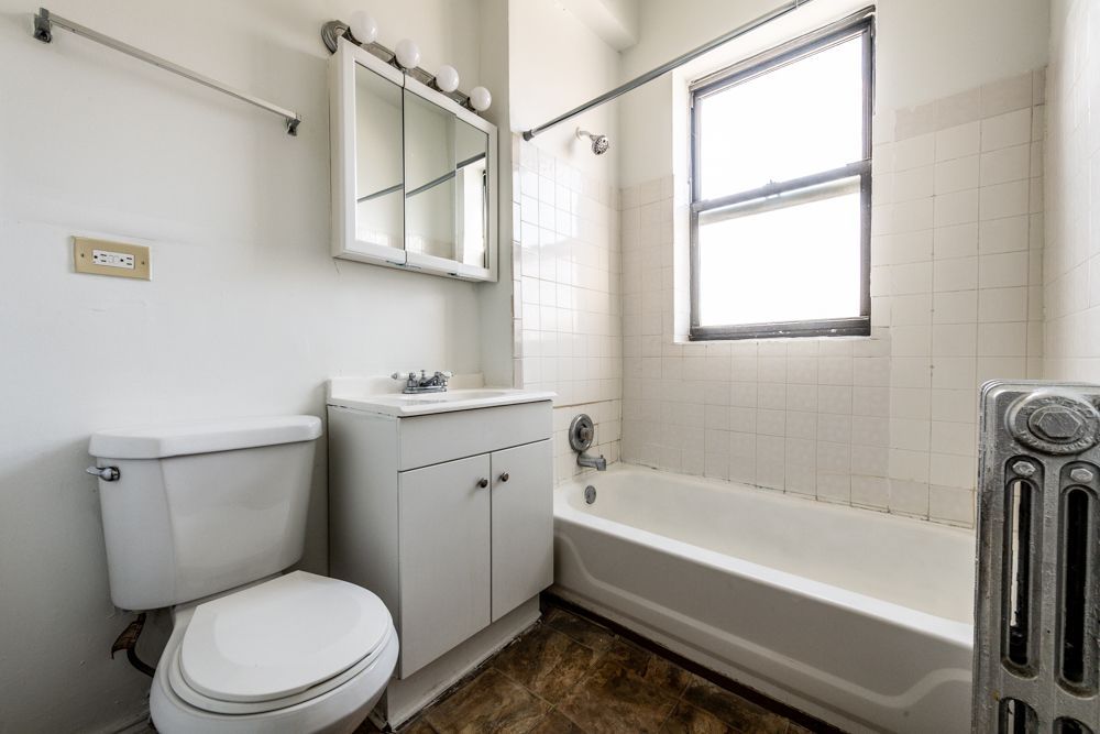 Bathroom with white fixtures, a window, and a radiator.
