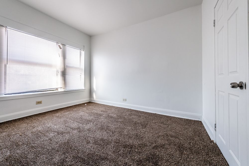 Empty room with brown carpet, white walls, a closed door, and a window with blinds.
