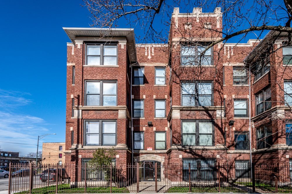 Brick apartment building with dark-framed windows, against a bright blue sky.