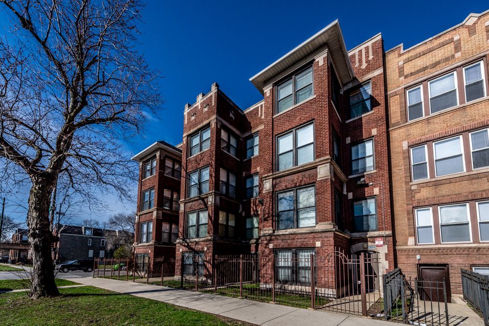 Brick apartment building with dark trim on a sunny day; tree and lawn in front.