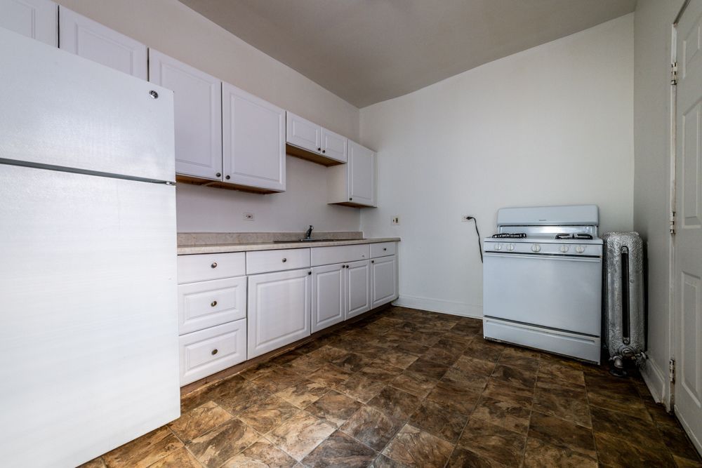 White kitchen with cabinets, refrigerator, and stove. Brown floor, white walls.