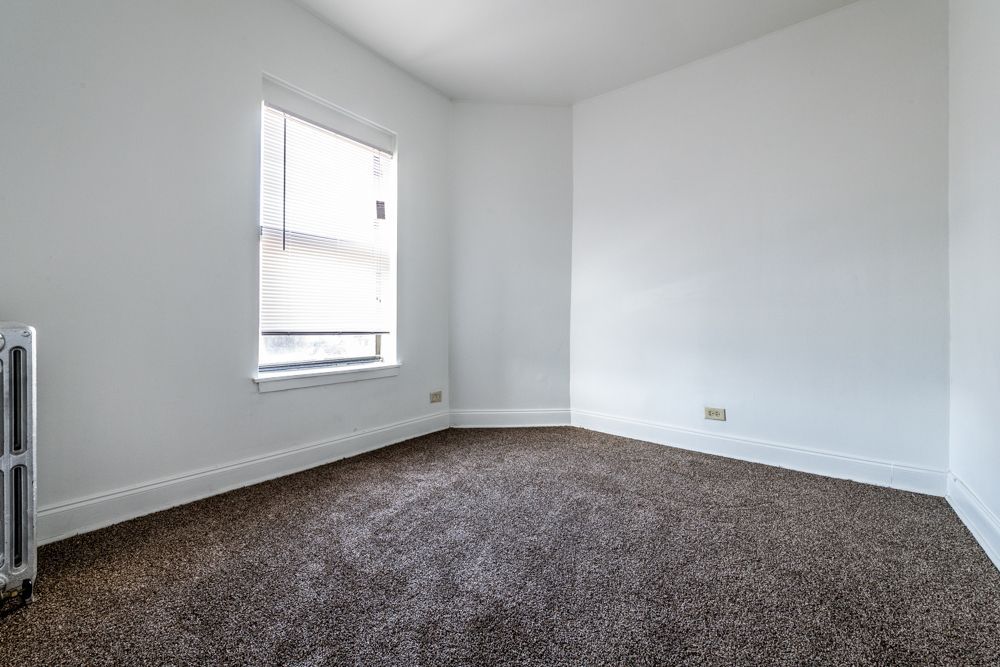 Empty room with brown carpet, white walls, small window, and radiator.