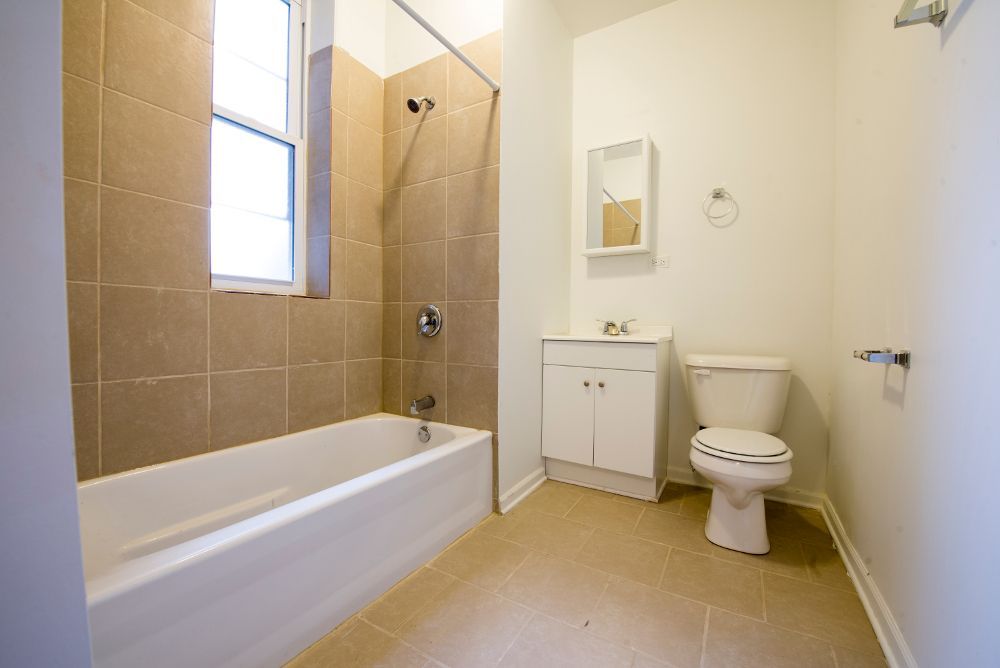 Bathroom with beige tile, white tub, toilet, and sink, and a small window.