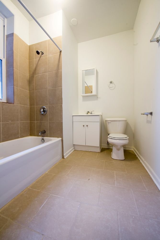 Bathroom with a white bathtub, toilet, and vanity against beige tile and flooring.