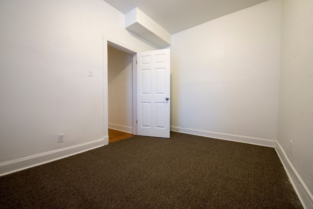 Empty room with brown carpet, white walls, and a partly open door.