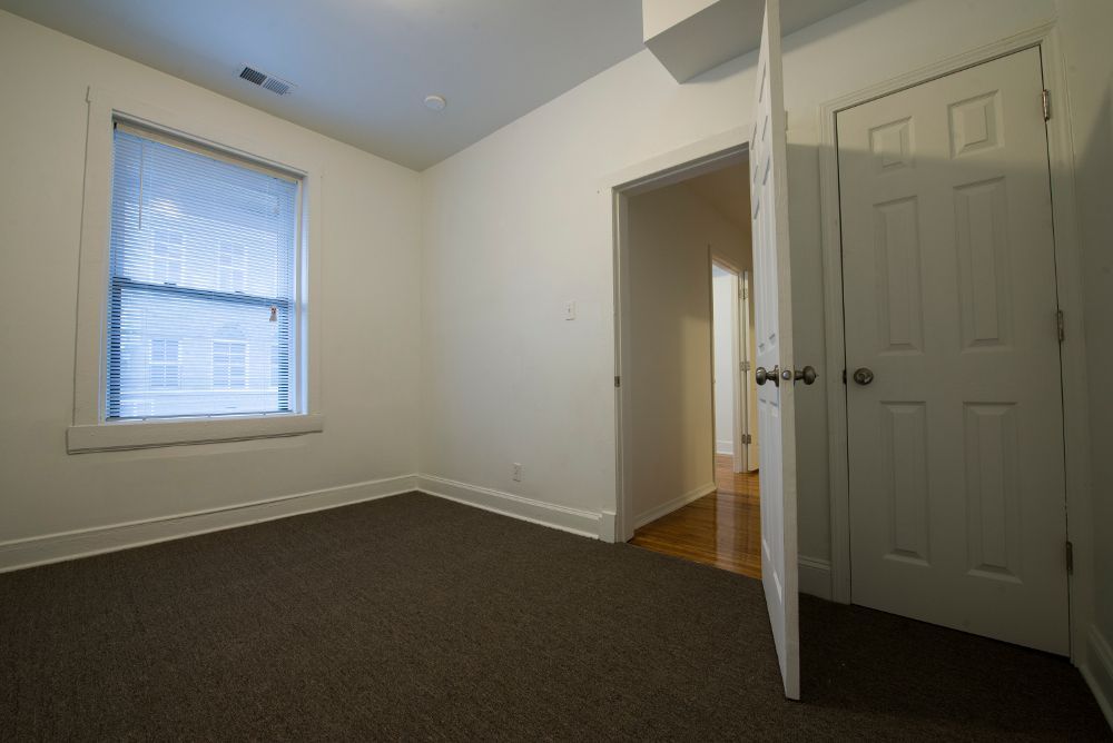 Empty room with brown carpet, white walls, window, open door to hallway.