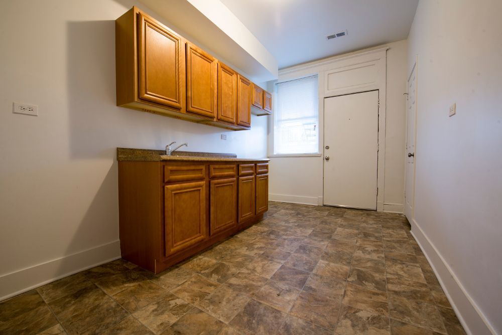 Kitchenette with wooden cabinets, countertop, and a door, in a room with linoleum flooring.