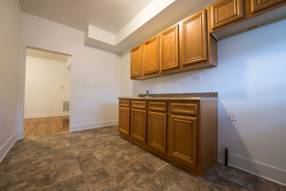 Empty kitchen with brown cabinets and countertop, gray flooring, and an open doorway.