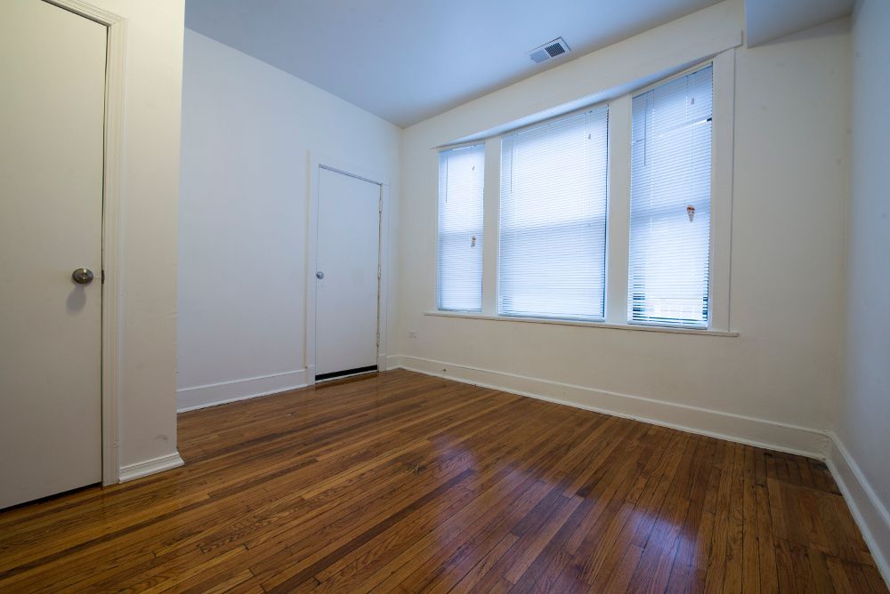 Empty room with wood floor, white walls, and a multi-pane window with blinds.
