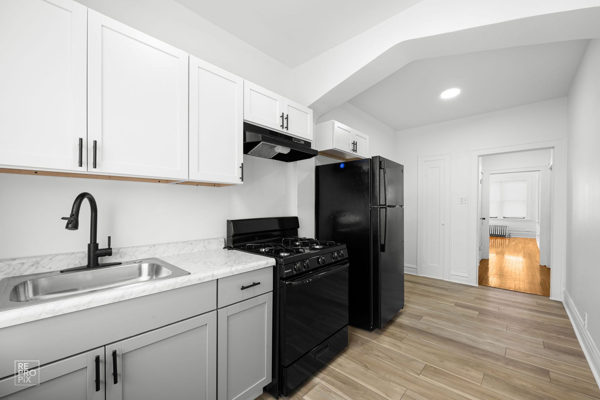 Small kitchen with white and gray cabinets, black appliances, and a light wood floor.
