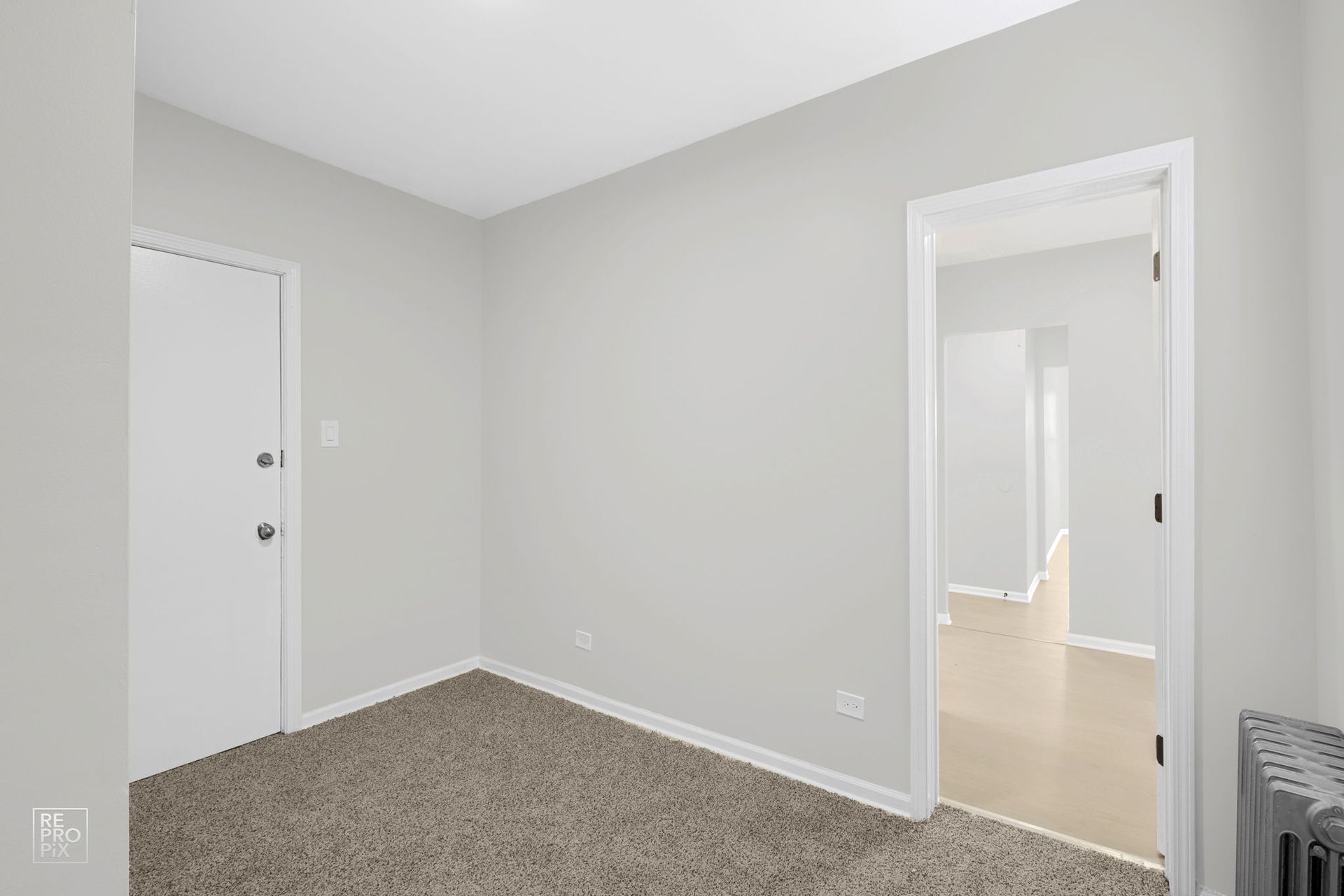 Empty room with gray walls, beige carpet, white door and doorway.